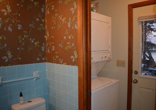 washroom featuring laundry area, wallpapered walls, and stacked washing maching and dryer