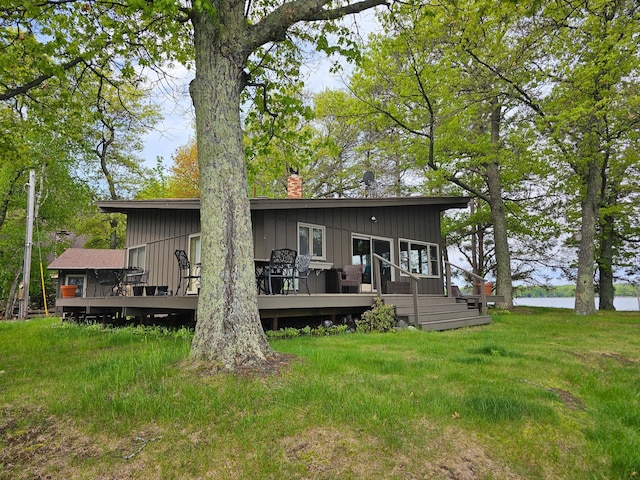 rear view of house featuring board and batten siding, a chimney, a deck with water view, and a yard