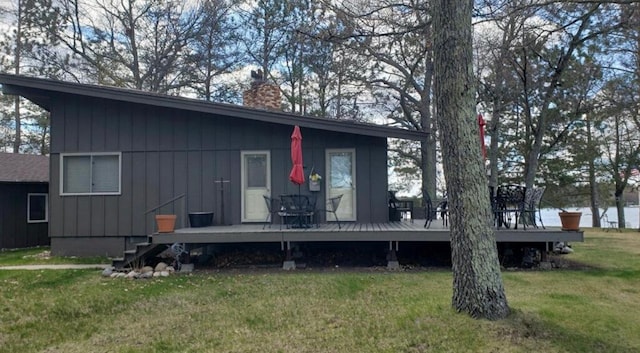 rear view of house featuring a chimney, a lawn, board and batten siding, and a wooden deck