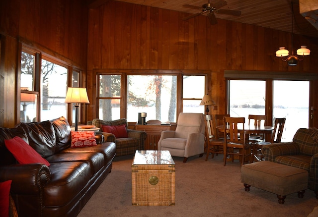 carpeted living area with high vaulted ceiling, wood walls, and a ceiling fan