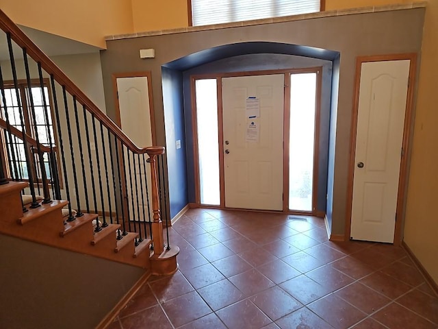 foyer entrance featuring tile patterned flooring, stairway, arched walkways, and baseboards