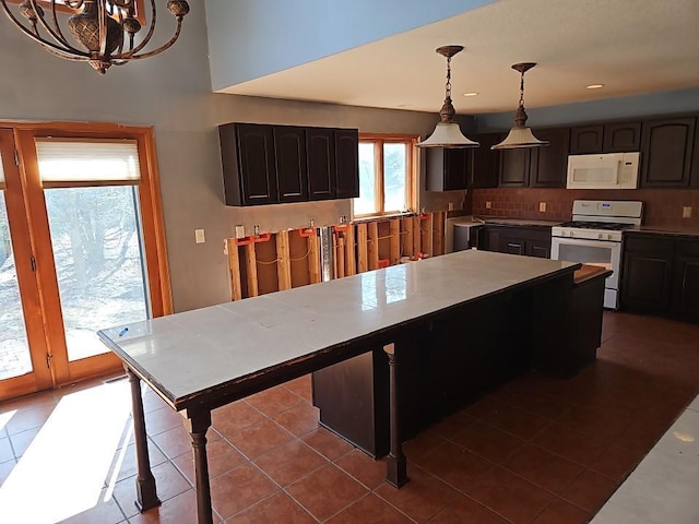 kitchen featuring dark tile patterned flooring, backsplash, white appliances, light countertops, and hanging light fixtures