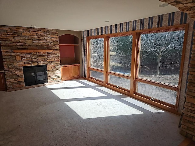 unfurnished living room with a stone fireplace, built in shelves, and concrete floors