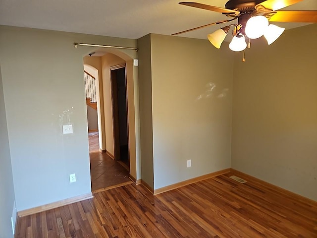 spare room with visible vents, baseboards, wood finished floors, arched walkways, and a ceiling fan