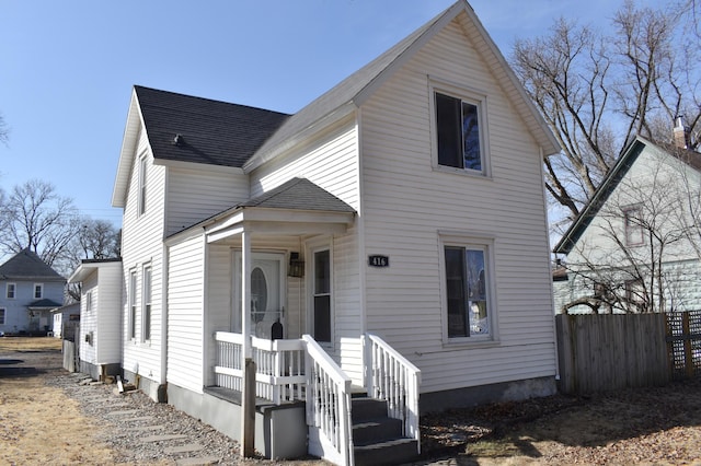 traditional home featuring covered porch, roof with shingles, and fence