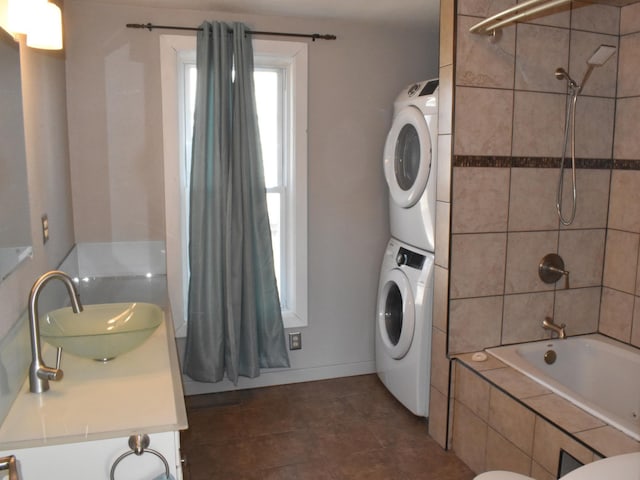 full bath featuring toilet, stacked washer and clothes dryer, tiled shower / bath combo, tile patterned floors, and vanity