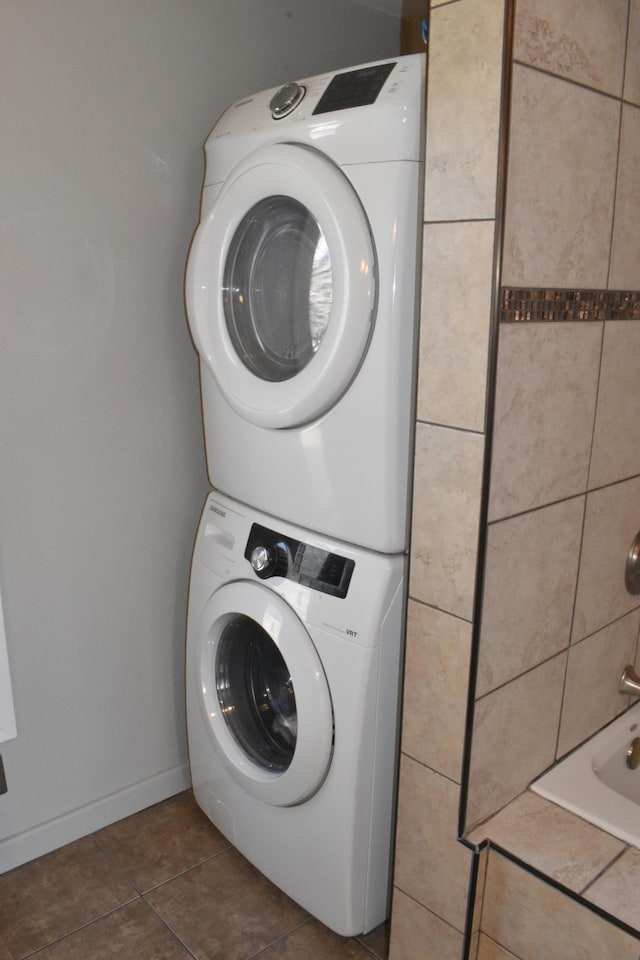 laundry room with baseboards, dark tile patterned floors, laundry area, and stacked washing maching and dryer