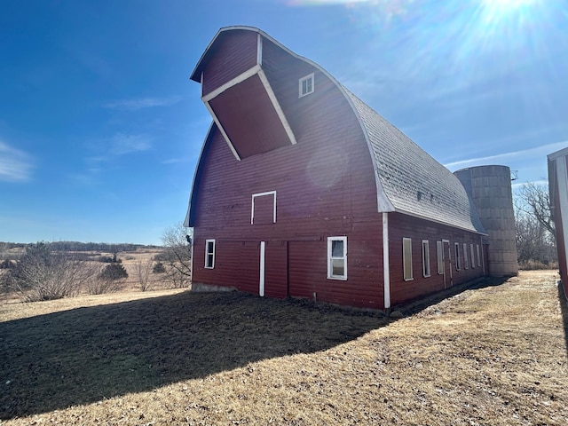 view of side of home with a gambrel roof, a barn, an outbuilding, and roof with shingles