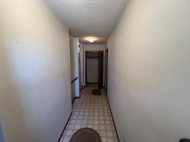 corridor with light floors, baseboards, and a textured ceiling