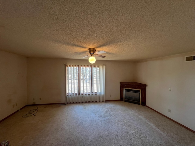 unfurnished living room with visible vents, a ceiling fan, a glass covered fireplace, carpet floors, and baseboards