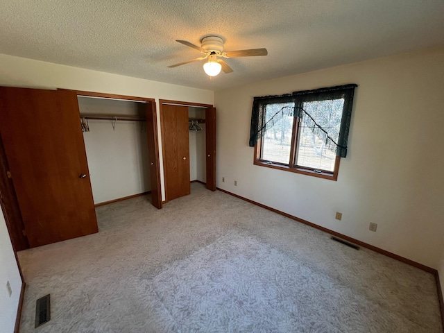 unfurnished bedroom with light carpet, visible vents, a textured ceiling, and multiple closets