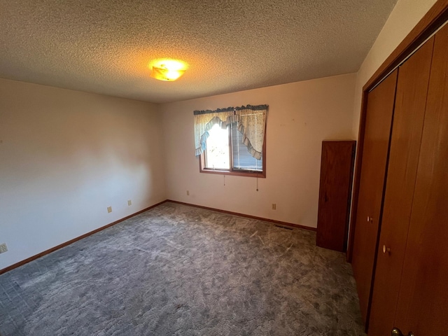 unfurnished bedroom featuring a closet, dark carpet, a textured ceiling, and baseboards