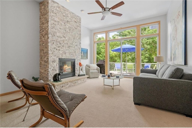 living area with a towering ceiling, carpet floors, a stone fireplace, baseboards, and ceiling fan