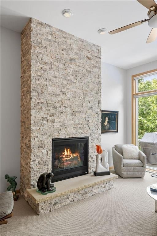 living area with carpet floors, a stone fireplace, and ceiling fan