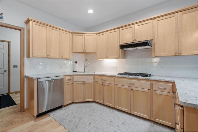 kitchen featuring light brown cabinets, under cabinet range hood, light stone counters, stainless steel appliances, and a sink