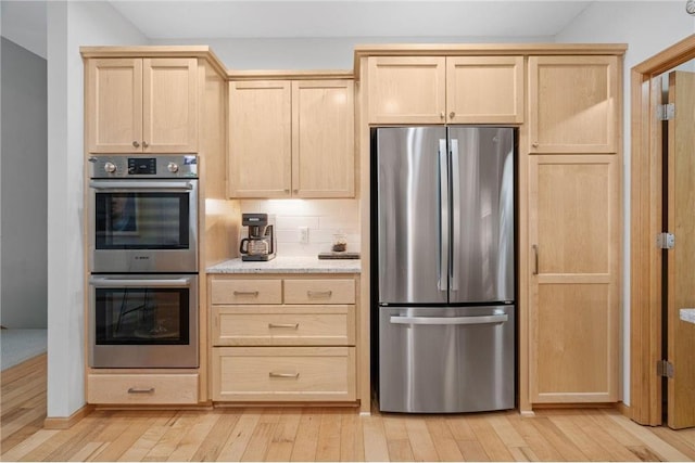 kitchen with light brown cabinets, light wood-style flooring, appliances with stainless steel finishes, and tasteful backsplash