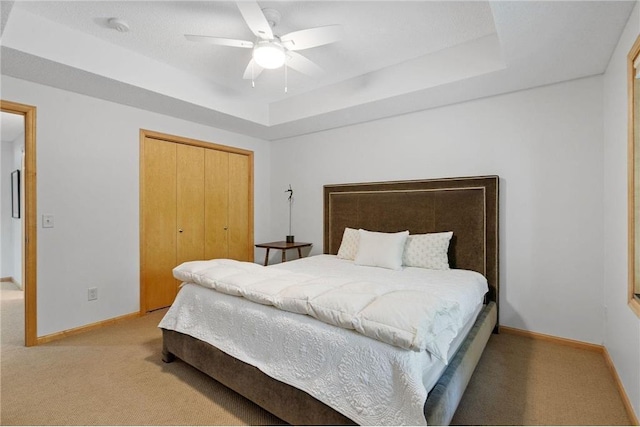 bedroom with light carpet, a tray ceiling, a closet, baseboards, and ceiling fan