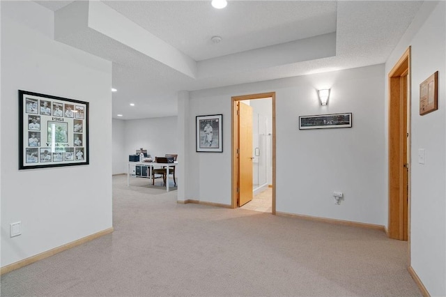 corridor with a tray ceiling, baseboards, and light carpet