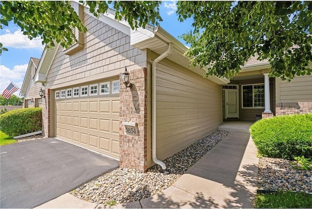 view of side of property featuring brick siding, an attached garage, and aphalt driveway