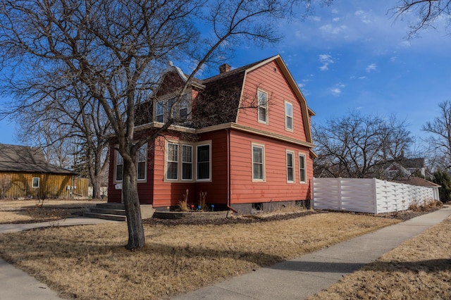 view of side of home with a gambrel roof, a chimney, and fence