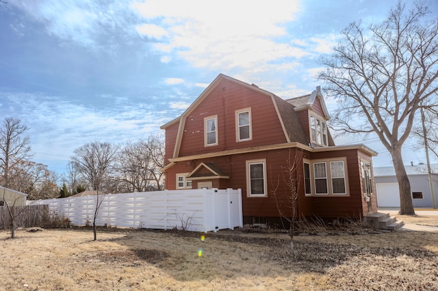 view of home's exterior with a gambrel roof, an outbuilding, roof with shingles, and fence private yard