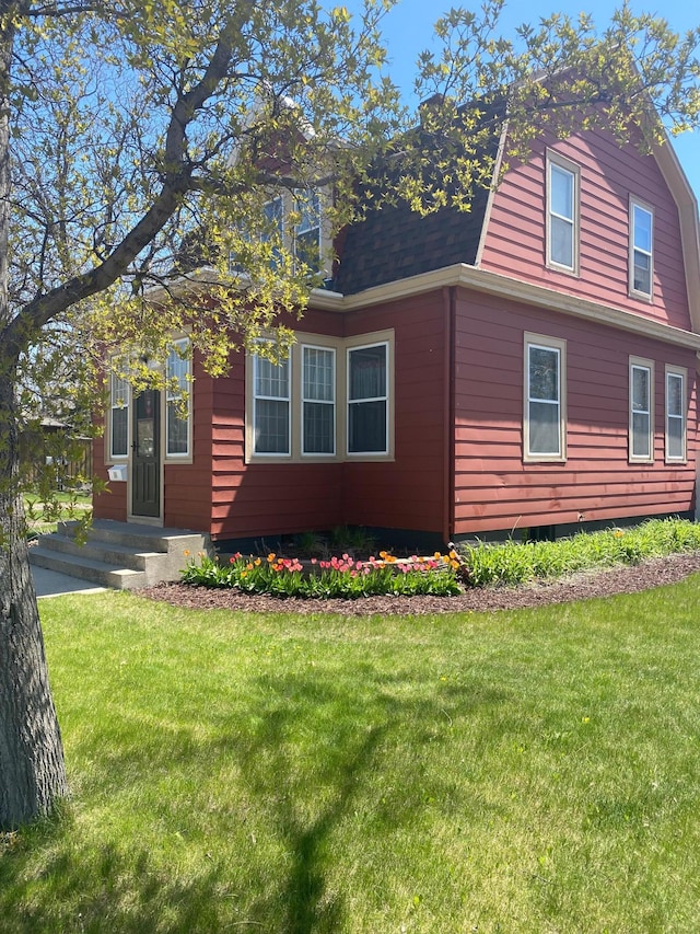 view of front of home featuring a gambrel roof, a shingled roof, and a front lawn