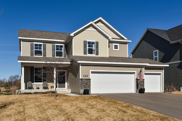 craftsman house featuring a shingled roof, a porch, a front yard, stone siding, and driveway