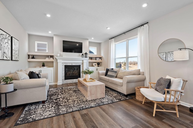 living area with a glass covered fireplace, baseboards, wood finished floors, and recessed lighting