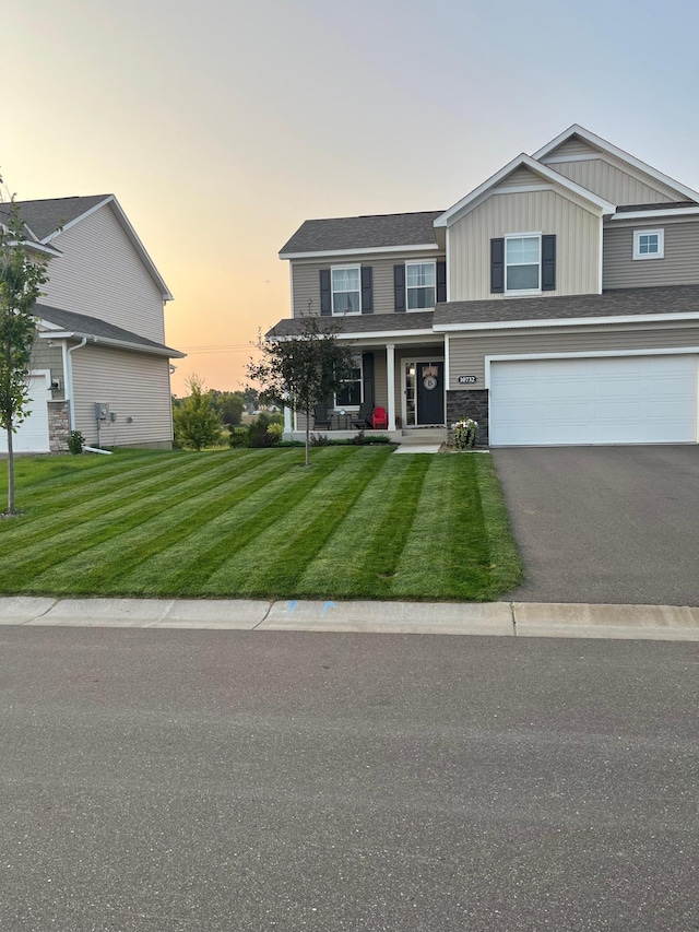 view of front of home featuring board and batten siding, aphalt driveway, a lawn, a garage, and stone siding