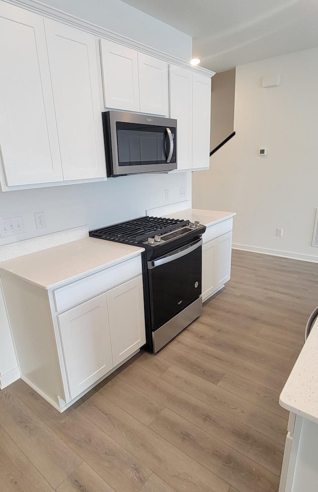 kitchen with light wood-type flooring, appliances with stainless steel finishes, white cabinetry, and light countertops