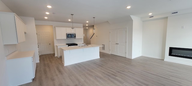 kitchen with visible vents, an island with sink, a sink, stainless steel microwave, and light wood finished floors