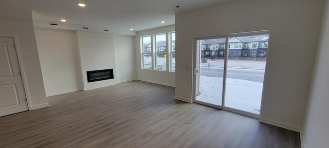 unfurnished living room featuring visible vents, wood finished floors, a glass covered fireplace, recessed lighting, and baseboards