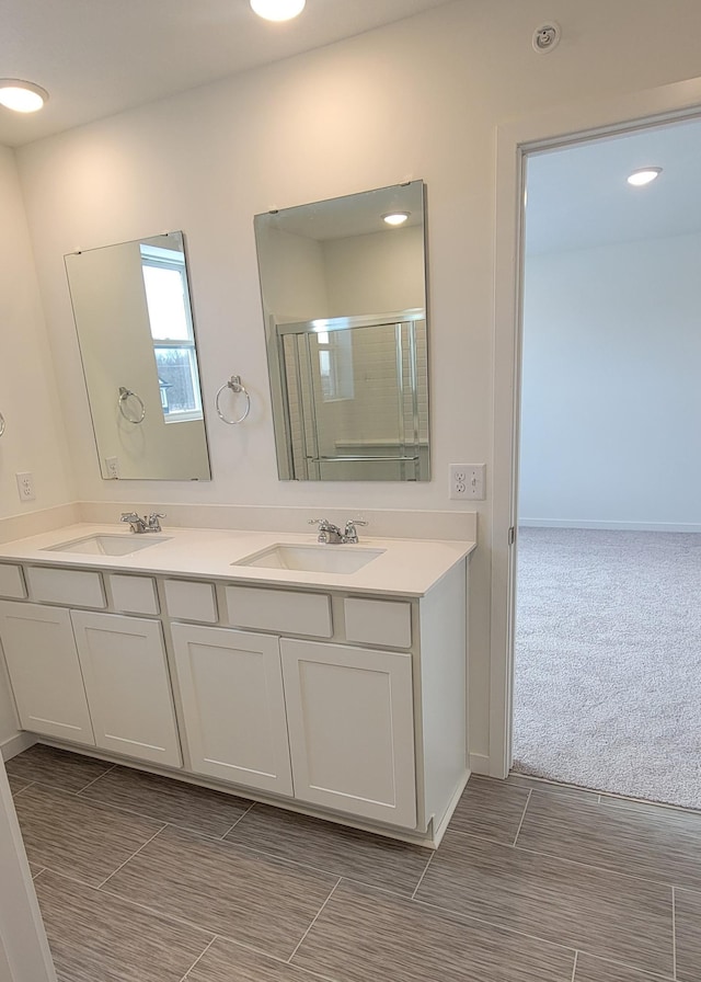 bathroom with double vanity, a shower with shower door, and a sink