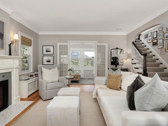 living area with crown molding, stairway, a fireplace with flush hearth, and light wood-type flooring