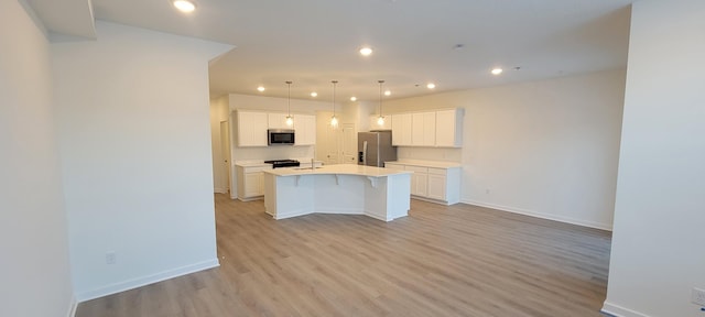 kitchen featuring light wood finished floors, appliances with stainless steel finishes, an island with sink, and baseboards