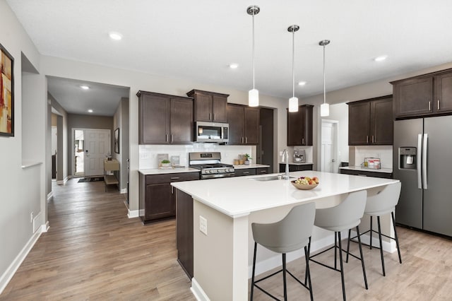 kitchen featuring tasteful backsplash, dark brown cabinets, an island with sink, stainless steel appliances, and a sink