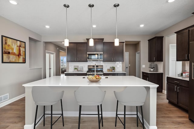 kitchen with tasteful backsplash, dark brown cabinets, a breakfast bar area, appliances with stainless steel finishes, and light wood-style floors