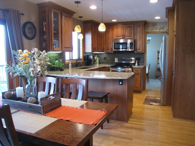 kitchen with a sink, stainless steel appliances, a peninsula, light wood finished floors, and decorative backsplash