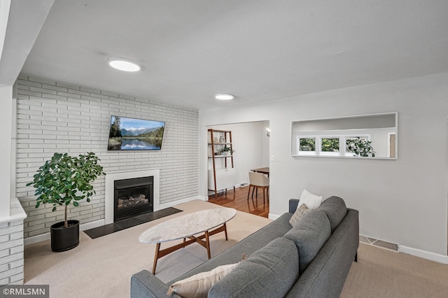 carpeted living room with visible vents, baseboards, brick wall, and a fireplace