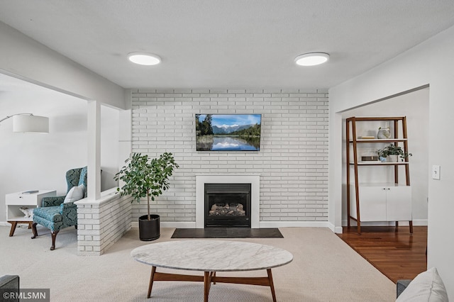 living room with a brick fireplace, a textured ceiling, and wood finished floors