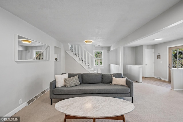 living area with stairway, light colored carpet, visible vents, and baseboards