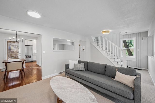 living area with stairway, wood finished floors, baseboards, carpet floors, and a notable chandelier