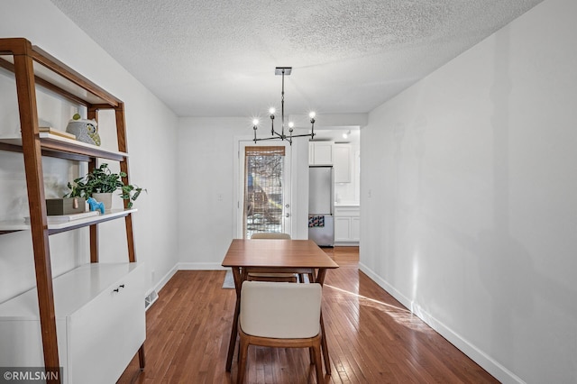 dining area featuring hardwood / wood-style floors, visible vents, baseboards, a textured ceiling, and a chandelier