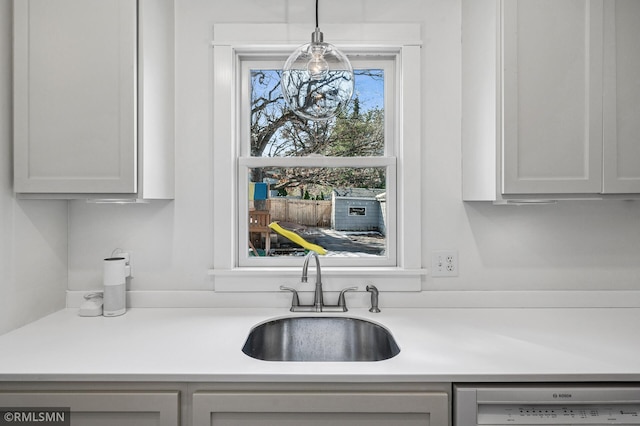 kitchen featuring decorative light fixtures, dishwasher, light countertops, and a sink