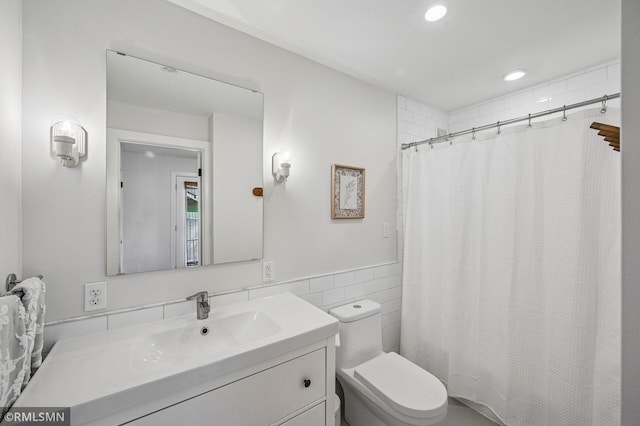 bathroom featuring a wainscoted wall, toilet, vanity, recessed lighting, and tile walls