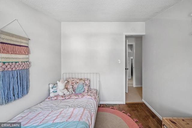 bedroom with wood finished floors, baseboards, and a textured ceiling