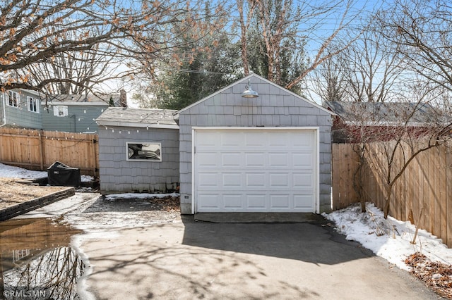 snow covered garage with a detached garage, concrete driveway, and fence