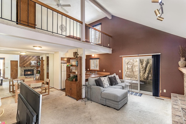 carpeted living area with beam ceiling, high vaulted ceiling, a ceiling fan, a stone fireplace, and baseboards