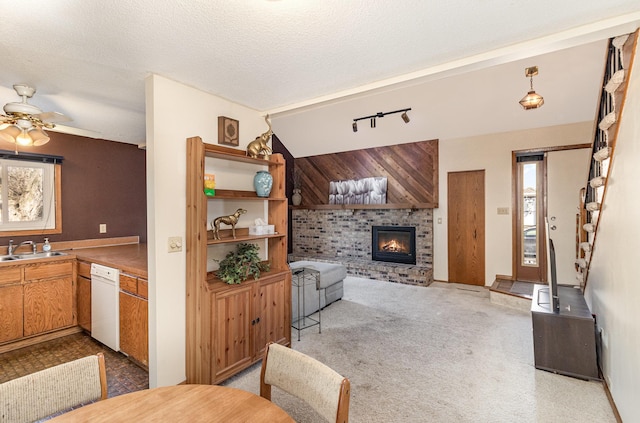 living room featuring light carpet, ceiling fan, rail lighting, a textured ceiling, and a brick fireplace