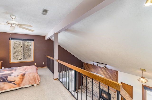 bedroom featuring visible vents, a textured ceiling, a glass covered fireplace, carpet, and vaulted ceiling with beams